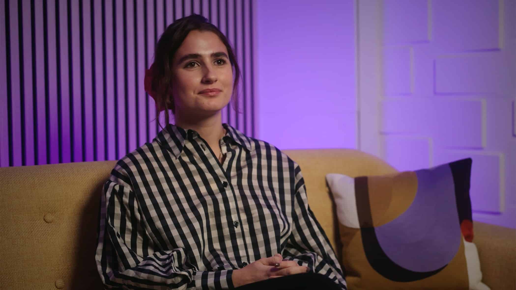 A woman sat on a sofa speaking to camera